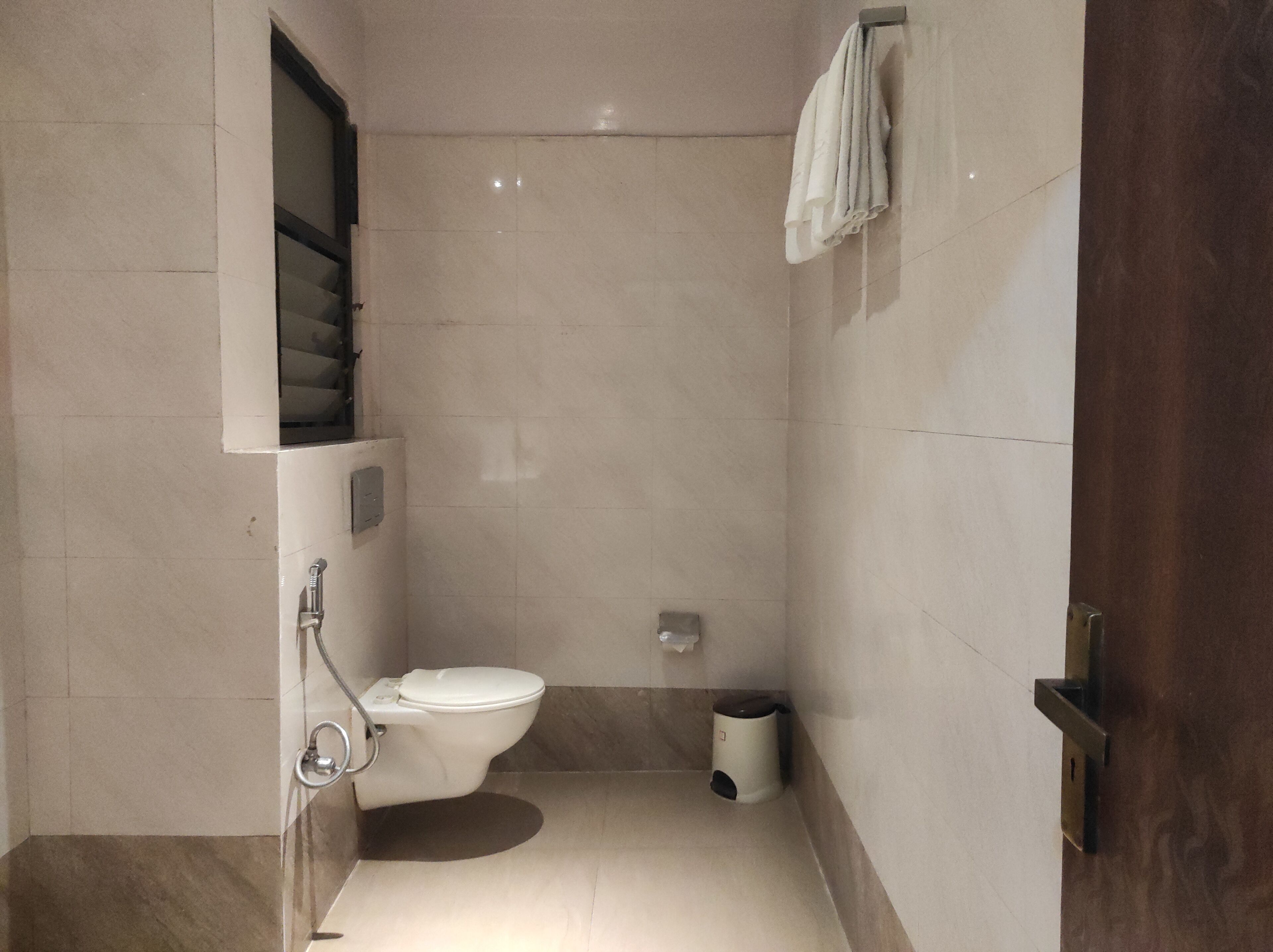 A small, modern bathroom with a toilet, a trash bin, and a towel rack.
