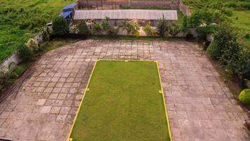 A rectangular paved area with a central grassy field, surrounded by a low stone wall and vegetation.