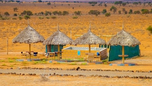 Una estructura con techo de paja y un pequeño edificio contiguo, ambos con asientos al aire libre y vistas del paisaje circundante.