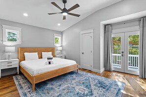 A bedroom with a wooden bed, white bedding, a blue patterned rug, a ceiling fan, and a view of the outdoors through a sliding glass door. - Endless Sunset - 30A, Heated Private Pool, Fire Pit, Steps to the Sand! (Santa Rosa Beach)