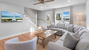 A spacious living room with a grey sectional sofa, a wooden coffee table, and a staircase leading to another level. - Endless Sunset - 30A, Heated Private Pool, Fire Pit, Steps to the Sand! (Santa Rosa Beach)