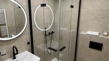 Un baño moderno con ducha envuelta en vidrio, lavamanos blanco y un inodoro.