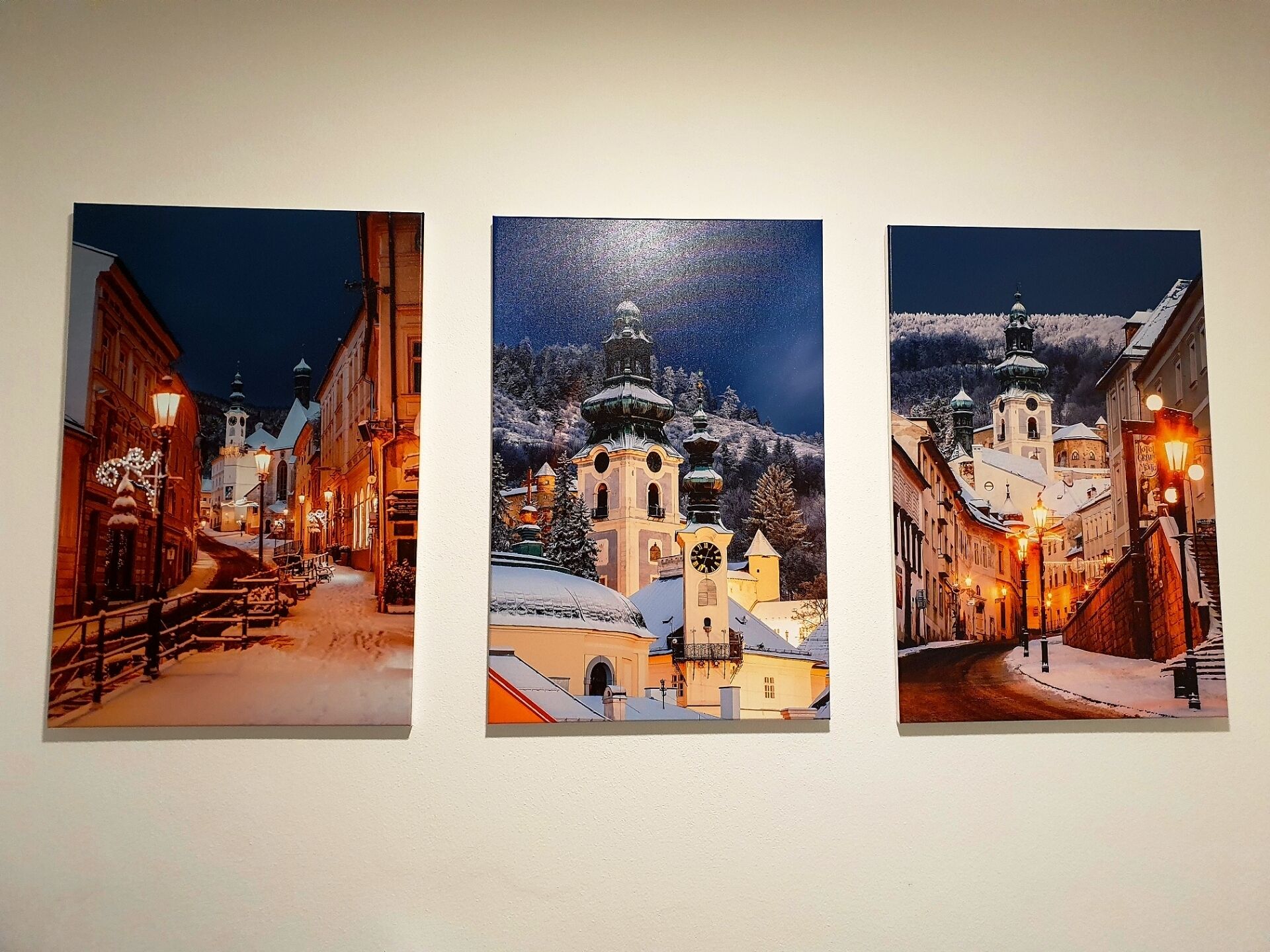 Three framed photographs of a snowy town street at night, featuring illuminated buildings and a church with a clock tower.