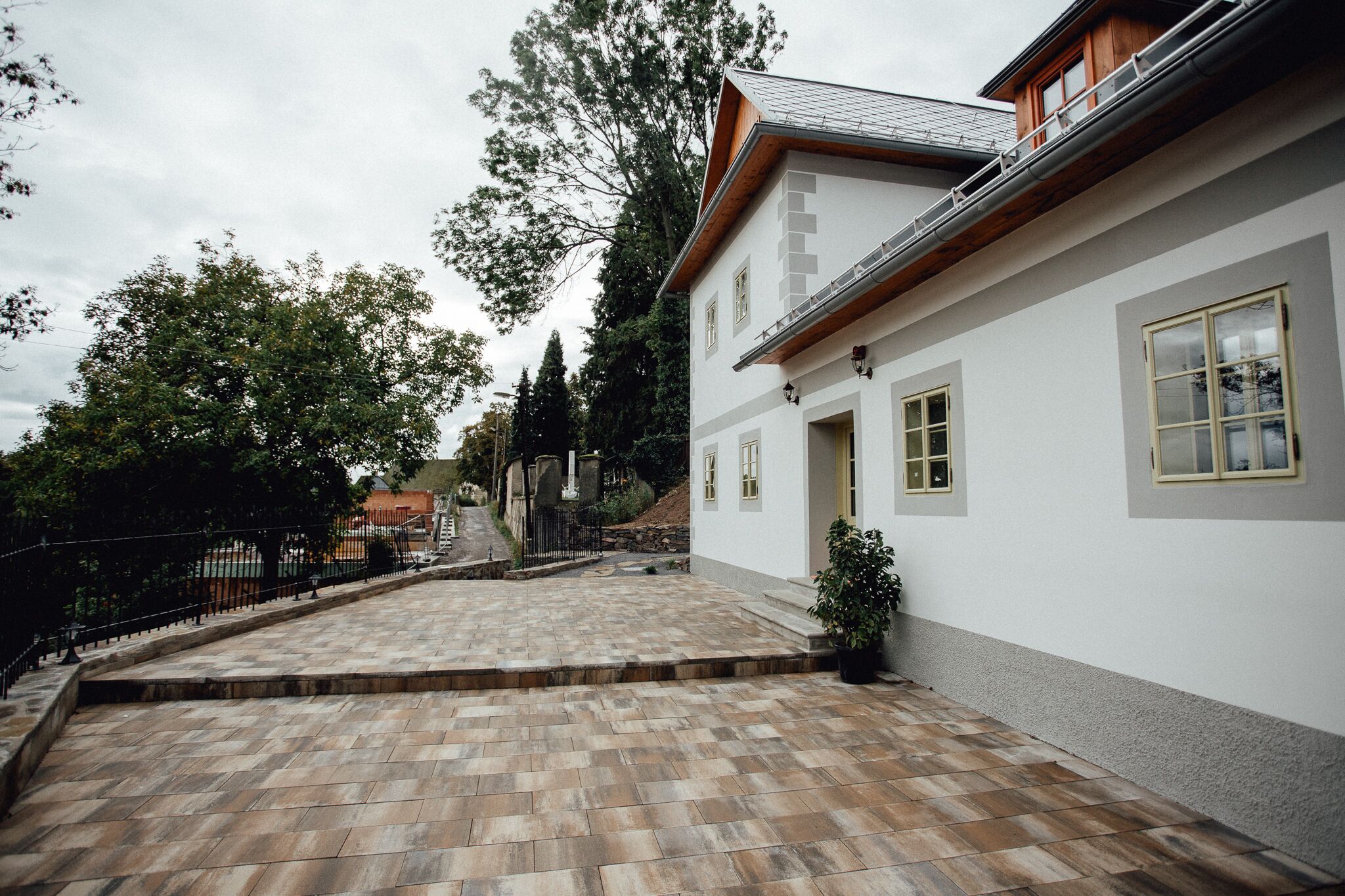 Una casa de dos pisos con un patio empedrado, una escalera de madera y una cerca de metal negro.
