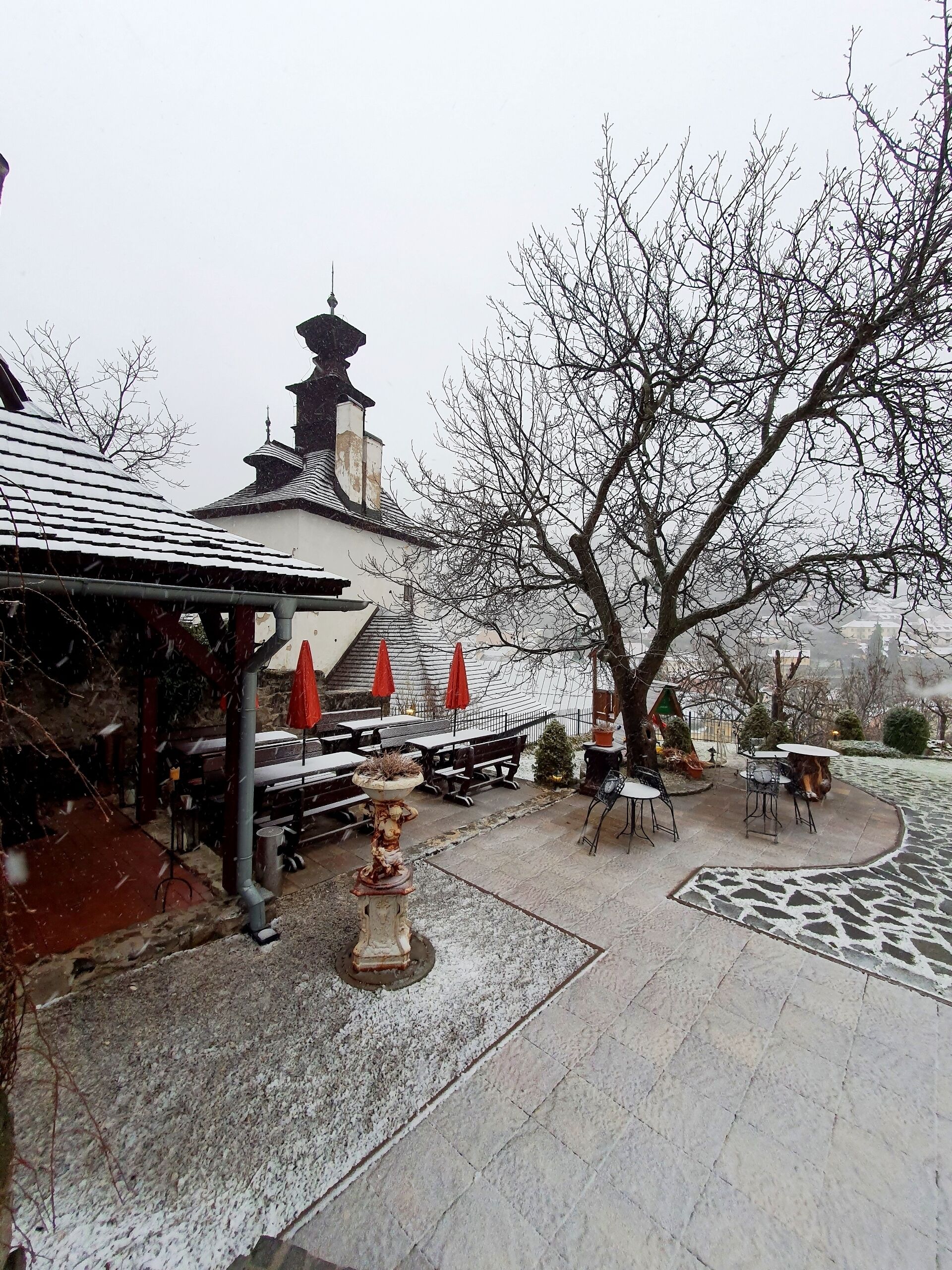 A traditional building with a pagoda-style roof, outdoor seating area with tables and chairs, and a large tree in the foreground.
