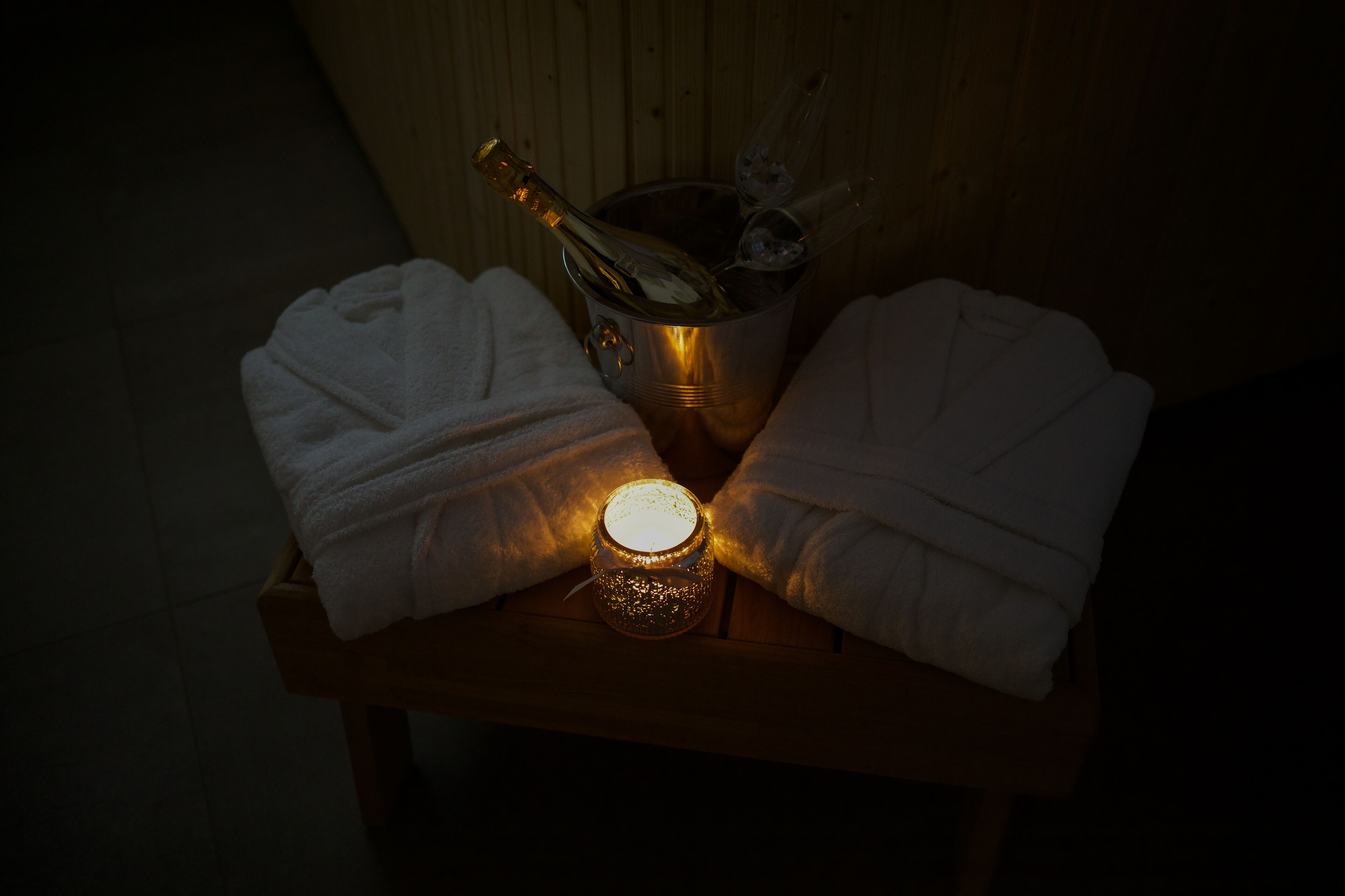 A wooden table with a bottle of champagne, two folded towels, and a lit candle.