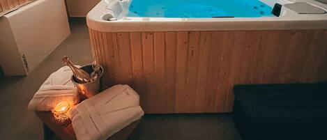 A room with a wooden bathtub, a small table with a candle, and a window.