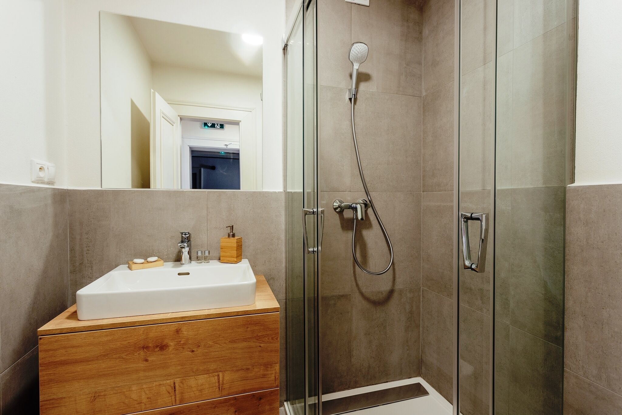 A modern bathroom with a glass-enclosed shower, a wooden vanity with a sink, and a mirror.
