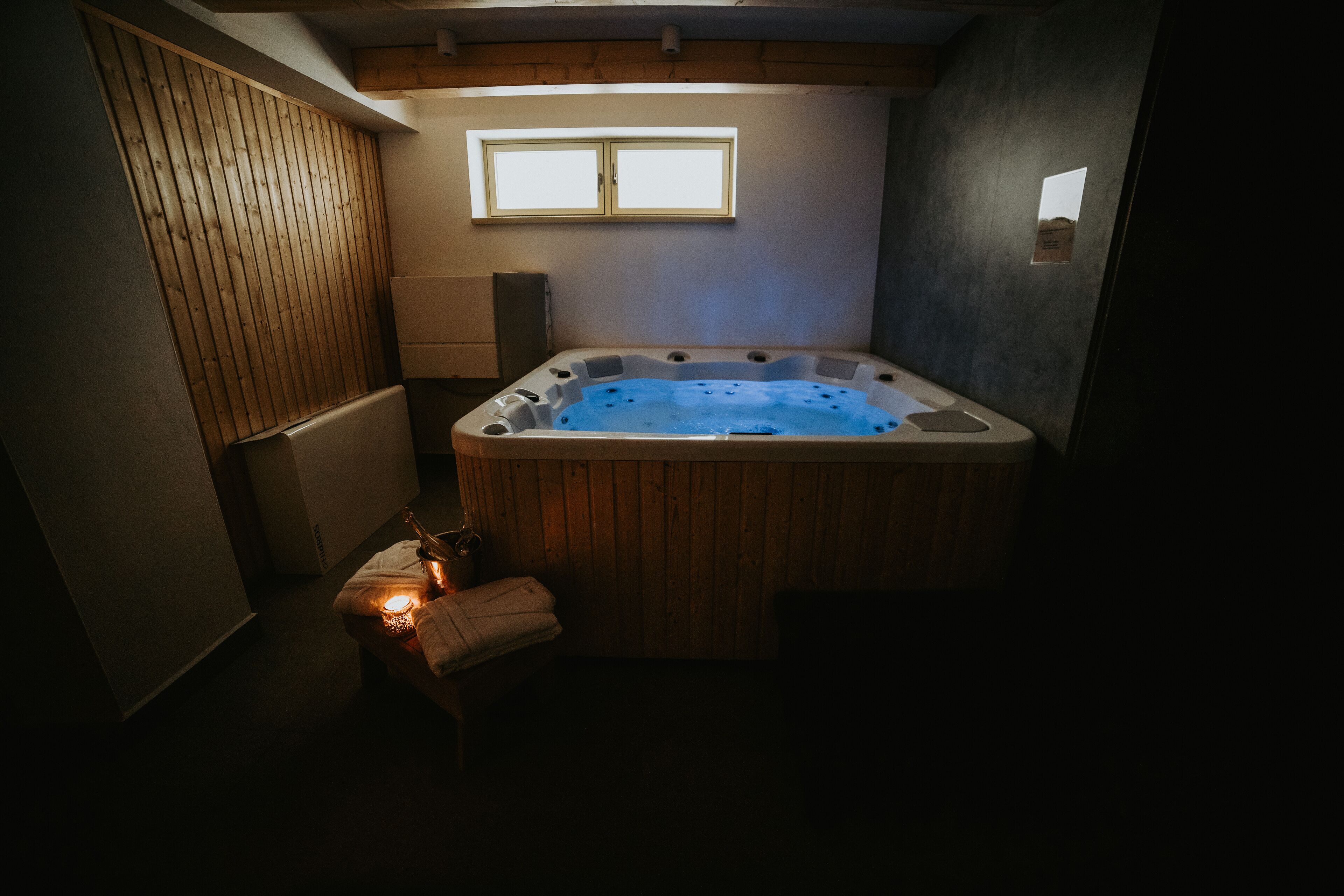 A hot tub in a dimly lit room with wooden paneling and a small window.