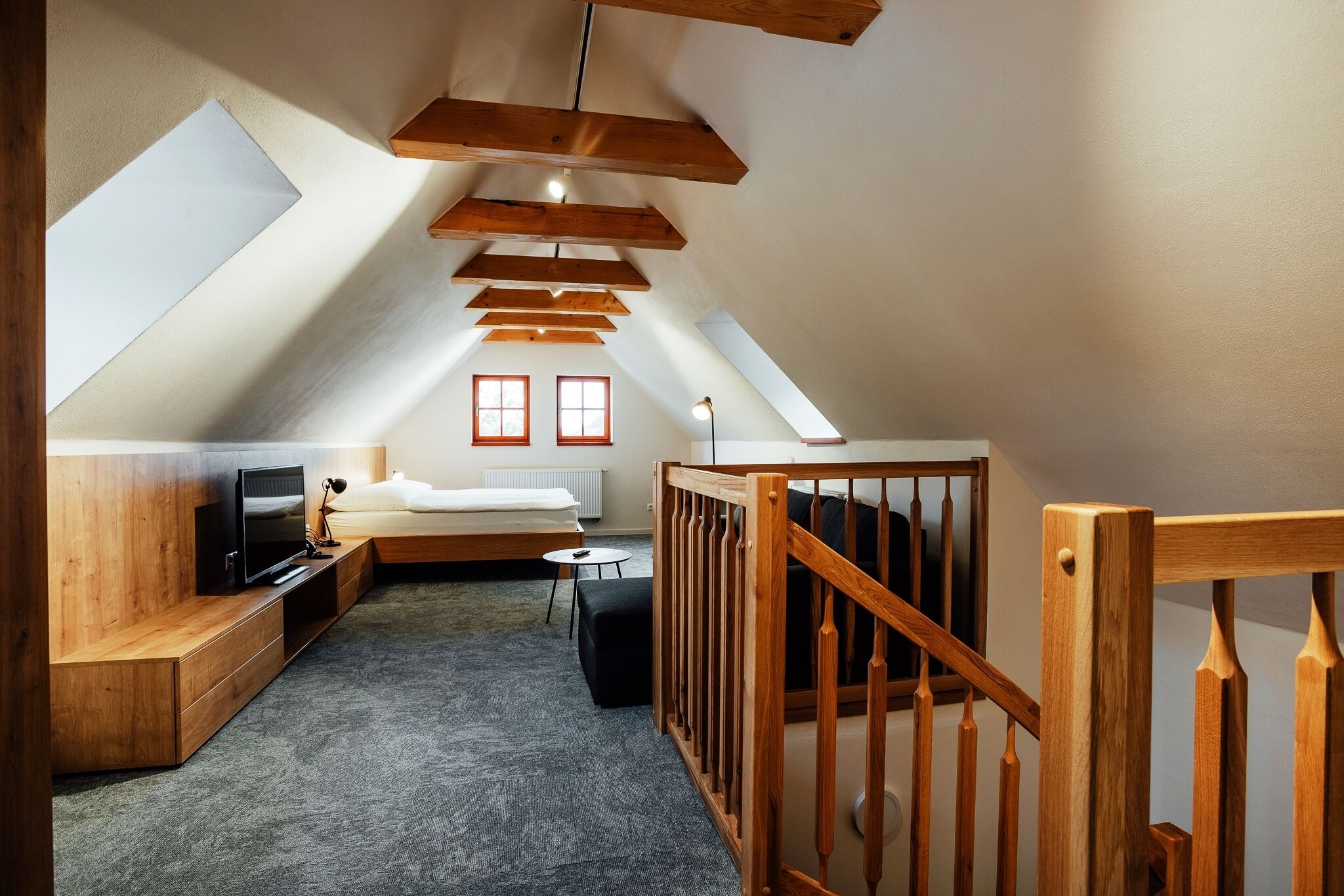 A cozy attic bedroom with a loft bed, wooden beams, a television, and a small seating area.