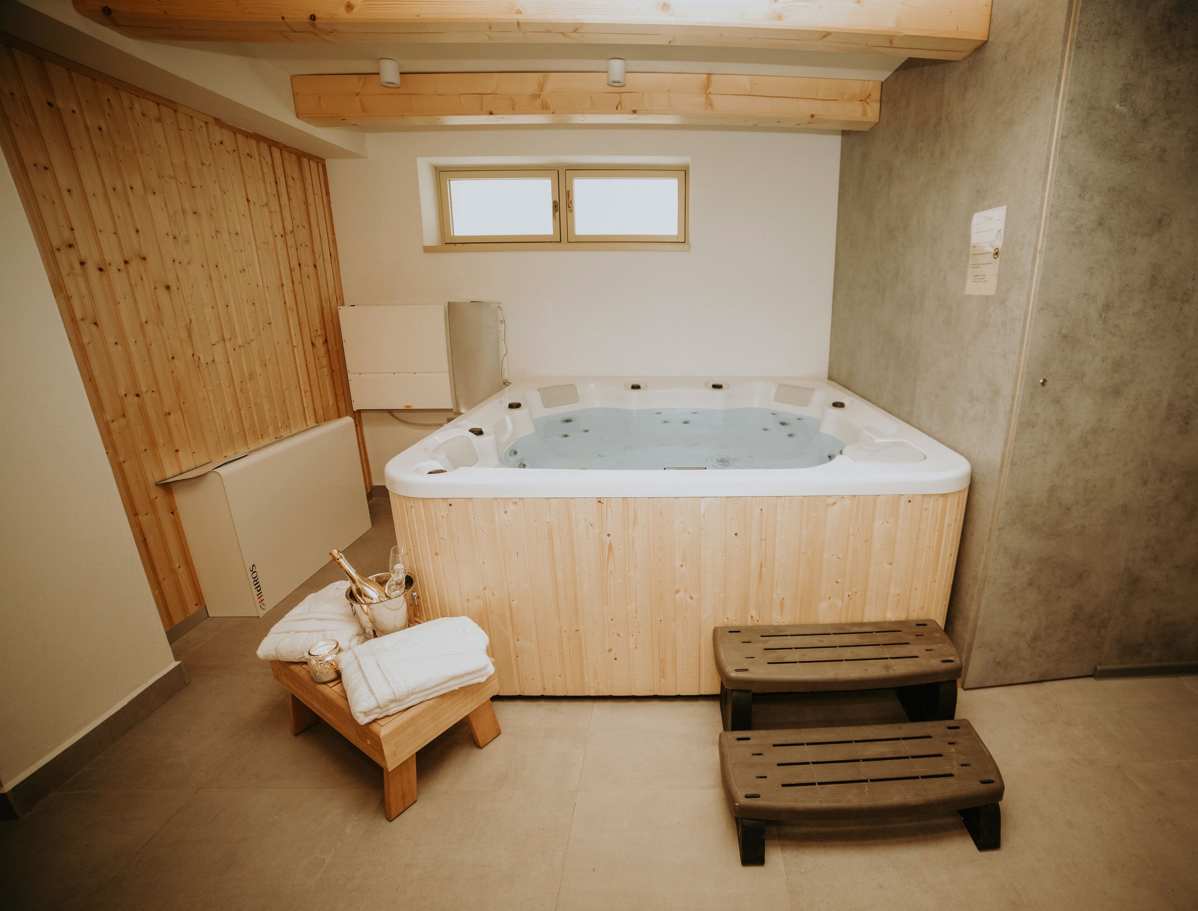 Een kamer met houten vloer, een jacuzzi, een bankje en een kleine tafel met handdoeken en een fles.