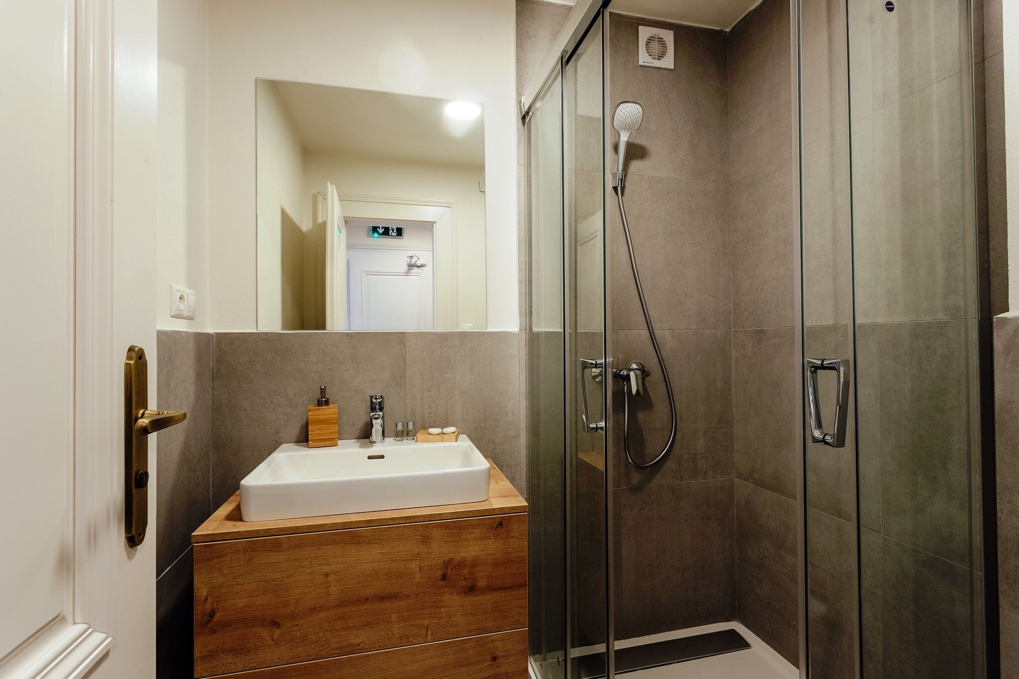 A modern bathroom with a wooden vanity, a glass shower enclosure, and a white sink.