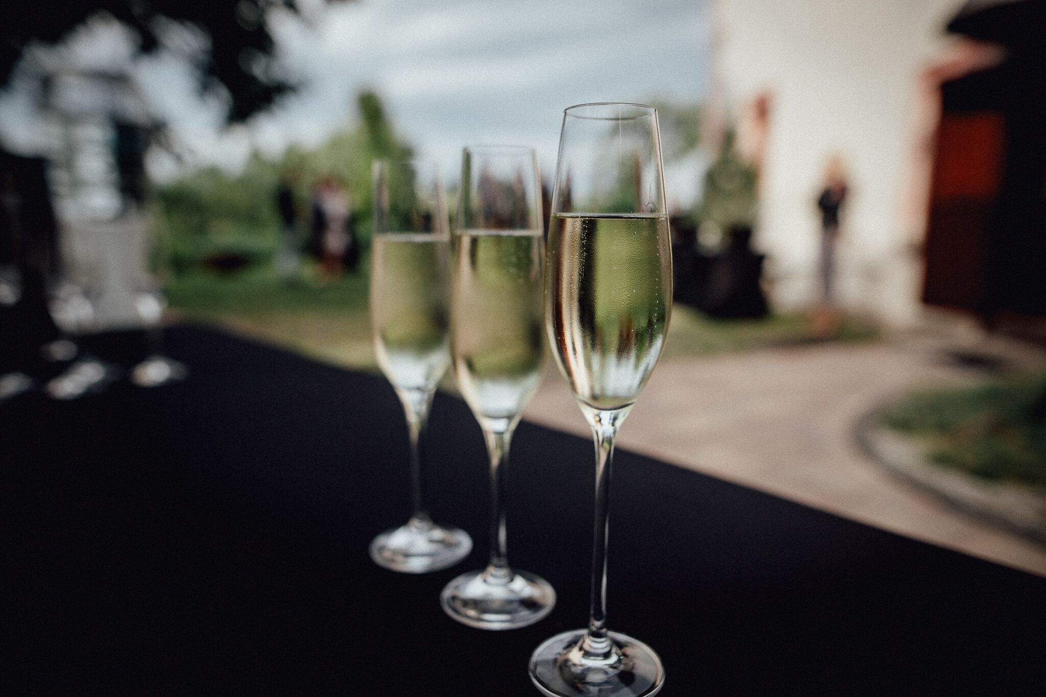 Three champagne flutes on a table with a blurred outdoor background.