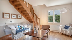 A spacious living room with a wooden staircase, a large window with a view of greenery, a white sofa, a coffee table, and a brown leather chair. - Charming house for 11 people in Sarzeau (Sarzeau)