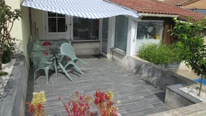 Une terrasse avec une table et des chaises, un espace abrité et des plantes en pot.