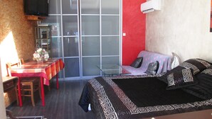 Une chambre d’hôtel comprenant un lit, un bureau, une chaise, une table avec un vase de fleurs et une porte-fenêtre coulissante donnant sur un espace extérieur.