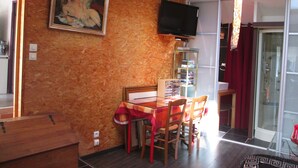 Un coin repas avec une table et des chaises, un tableau accroché au mur, un téléviseur fixé au-dessus de la table et une porte vitrée donnant sur l’extérieur.