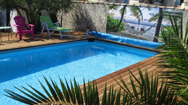 Une piscine dot ée d’une terrasse en bois, entourée de palmiers et de chaises longues.