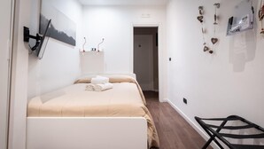 Un dormitorio con una cama, un escritorio y una silla. Hay una puerta que da a otra habitación.