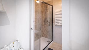 Un baño moderno con cabina de ducha de vidrio, sanitarios blancos y una alfombra de baño negra.