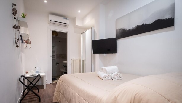 Habitación de hotel con cama, televisor montado en la pared, radiador y una mesita con artículos de aseo.