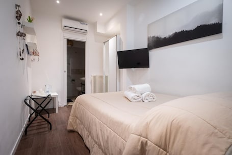 A hotel room with a bed, a TV mounted on the wall, a radiator, and a small table with toiletries.