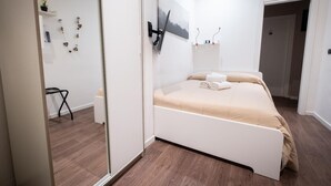 Un dormitorio moderno con cama, televisor montado en la pared y una pequeña mesa con silla.