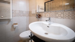 Un baño con lavamanos blanco, inodoro, toallero y zona de ducha.