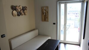 A room with a beige sofa, a black table, decorative wall art, and a sliding glass door leading to an outdoor area. - Cavour Room 5 Suite (Bari)