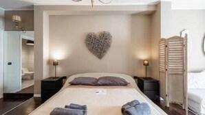A hotel room with a large bed, a heart-shaped wall decoration, two bedside tables with lamps, and a wooden wardrobe. - Cavour Room 5 Suite (Bari)