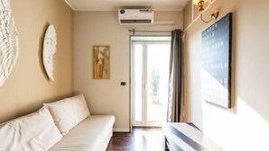 A room with a sofa, an air conditioning unit, a painting, and a wall-mounted light fixture. - Cavour Room 5 Suite (Bari)
