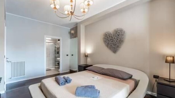 A bedroom with a large bed, a heart-shaped wall decoration, and a chandelier. - Cavour Room 5 Suite (Bari)
