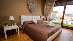 A bedroom with a large bed, a bedside table with a lamp, a heart-shaped wall decoration, and a view of the outdoors. - SWEET EMOTIONS ROOM 81 (Bari)
