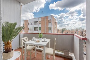 A balcony with a table, chairs, a potted plant, and a view of a multi-story building. - GuestHost - Bright Apartment with a Terrace (Ferrara)