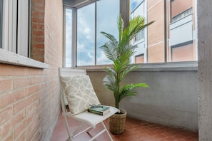 A balcony with a white chair, a potted plant, and a book.