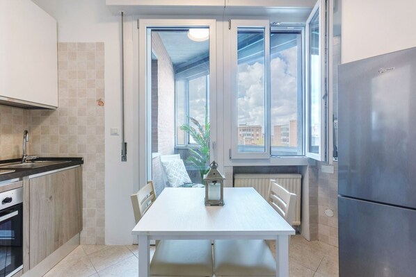 A compact kitchen with a dining table, a refrigerator, and a window with a view of buildings.