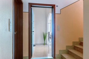 A hallway with a door leading to a room, a staircase, and a plant.