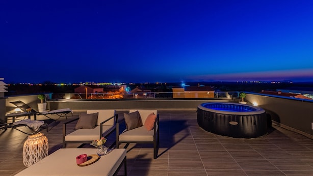 A rooftop terrace with outdoor seating, a hot tub, and a view of the city skyline at dusk. - Villa Tia (Policnik)