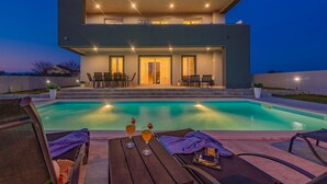 A modern two-story house with a swimming pool, outdoor seating, and a well-lit patio area. - Villa Tia (Policnik)