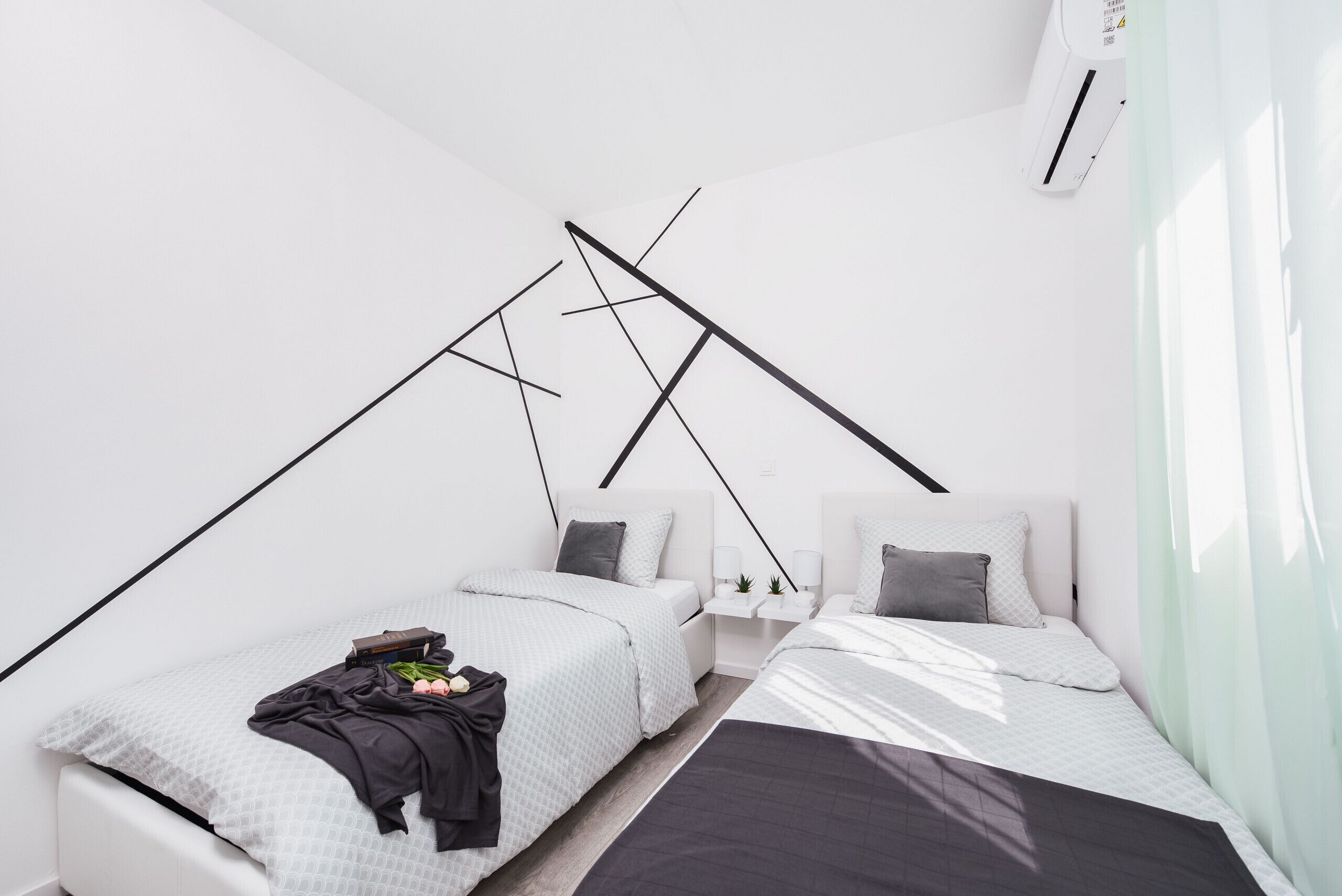 A modern, minimalist bedroom with two beds, a white wall, and a sloped ceiling.