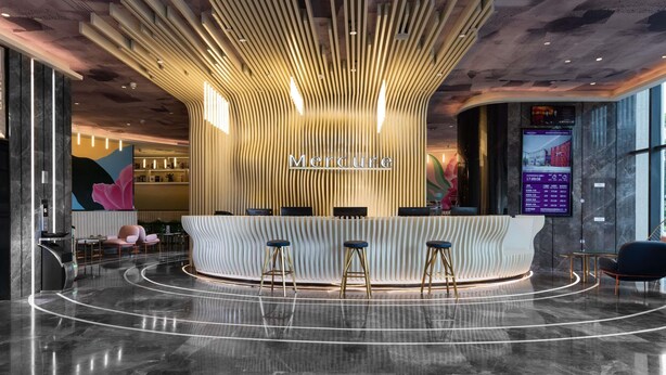 Un comptoir d’accueil au design moderne, doté d’un écran numérique et d’un espace détente avec des tabourets.