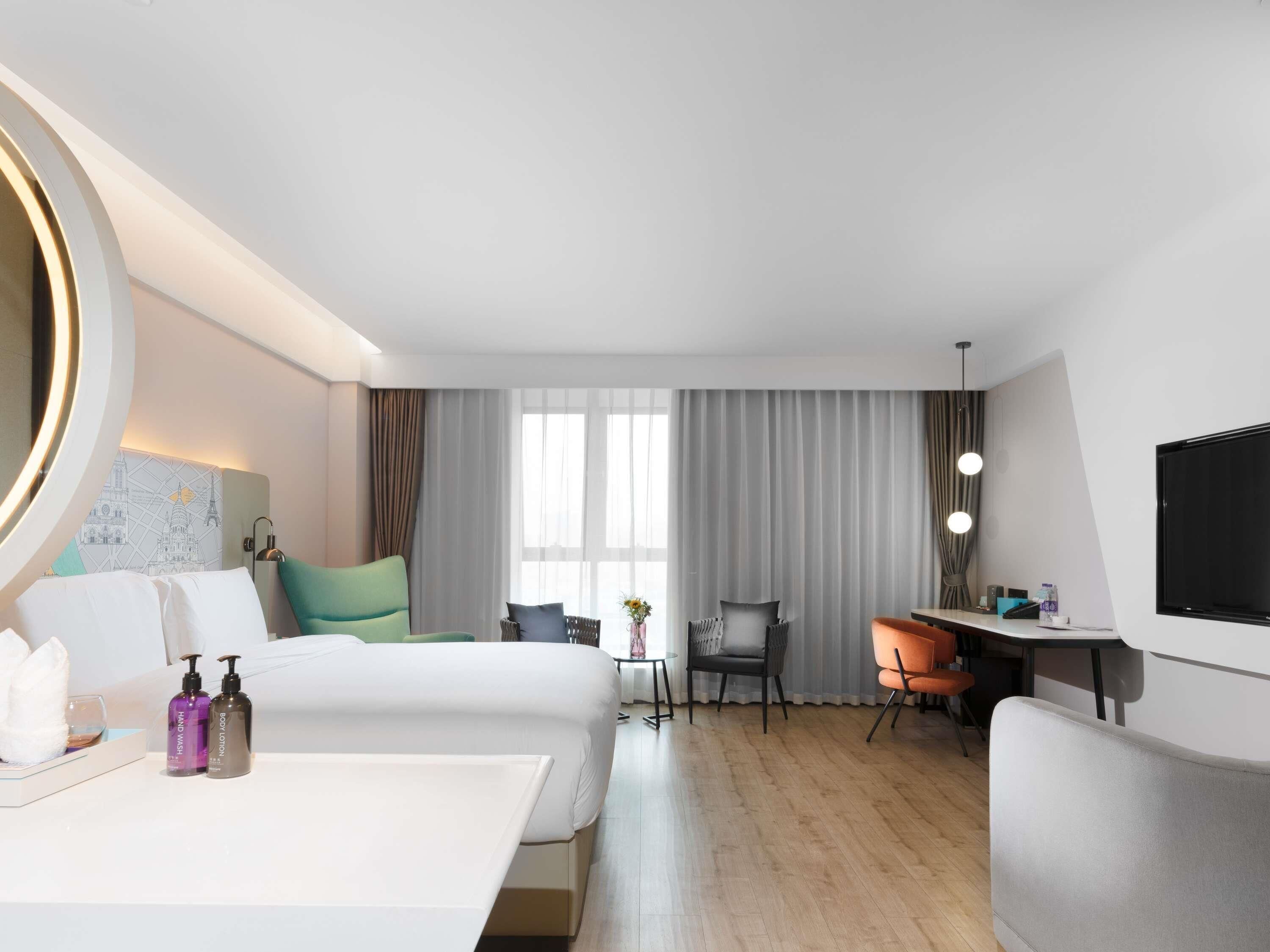 Una camera d'albergo con un letto, due poltrone, una scrivania, una televisione e una finestra con tende.