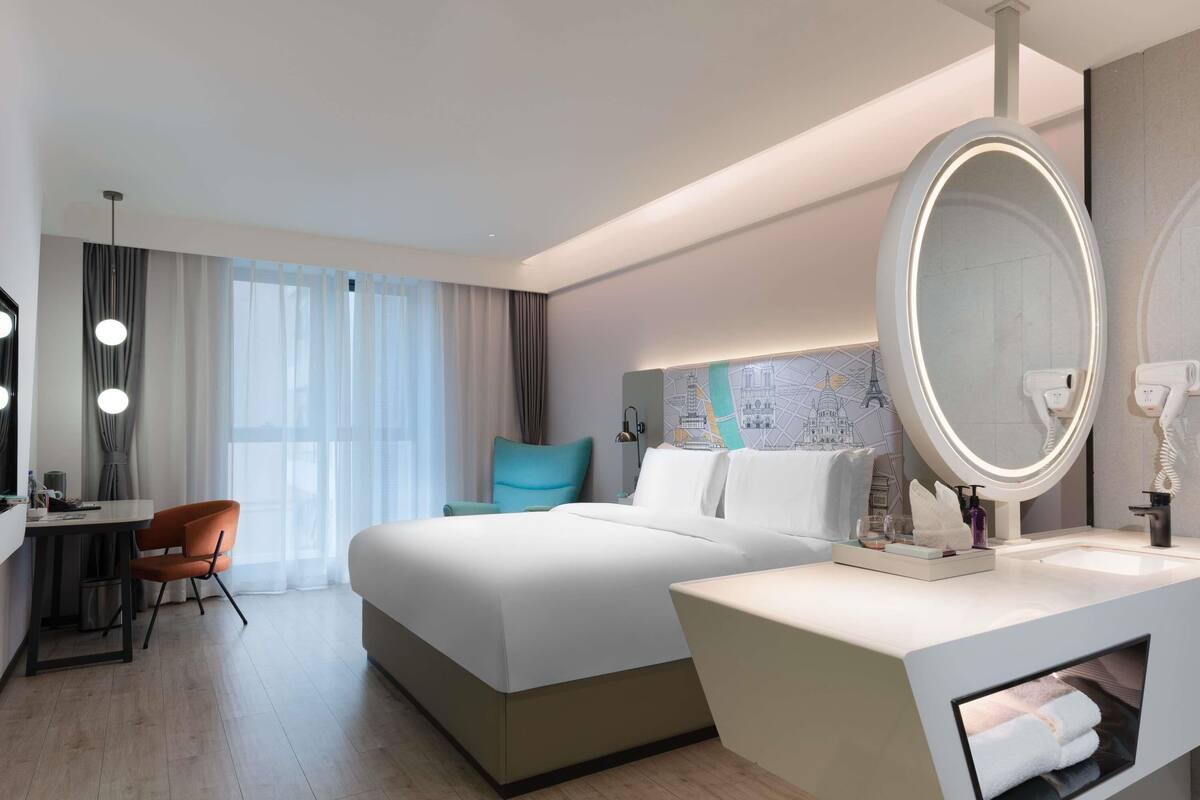 A hotel room with a bed, a desk, a chair, a large mirror, and a map on the wall.