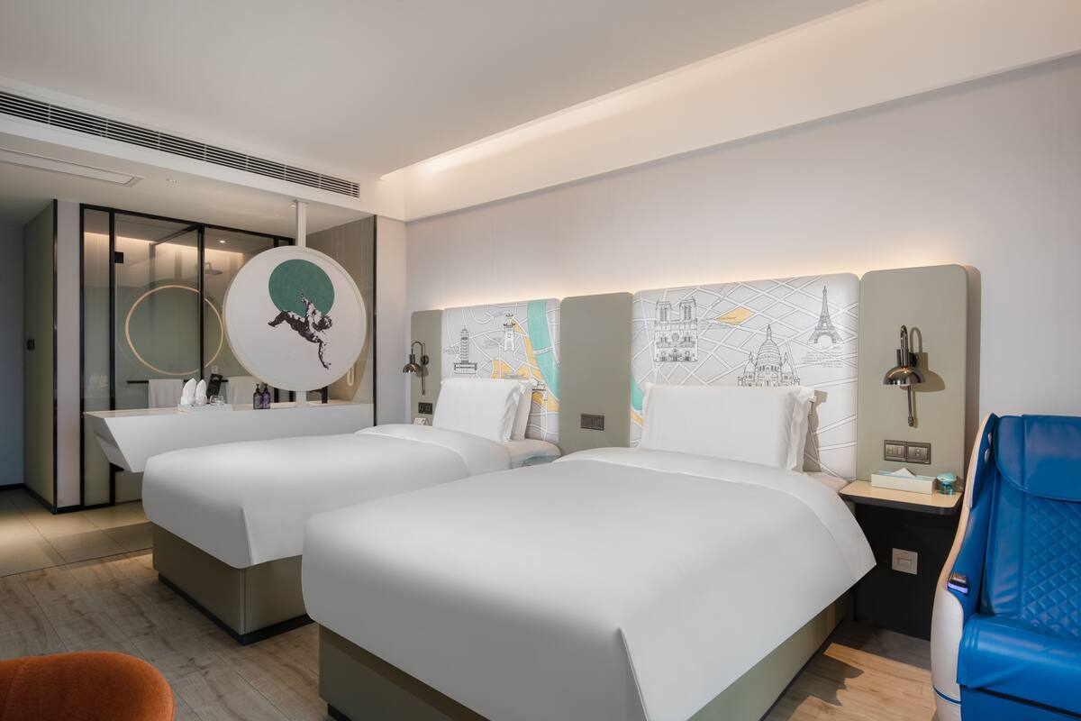 A hotel room with two beds, a desk, a chair, and a wall with a map design.