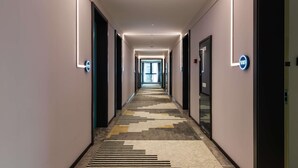 Un couloir d’hôtel avec un tapis à motifs, un éclairage moderne et des portes portant l’indication du numéro de chambre.
