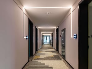 Un couloir dâhĂŽtel avec un tapis Ă motifs, un Ă©clairage moderne et des portes portant lâindication du numĂ©ro de chambre.