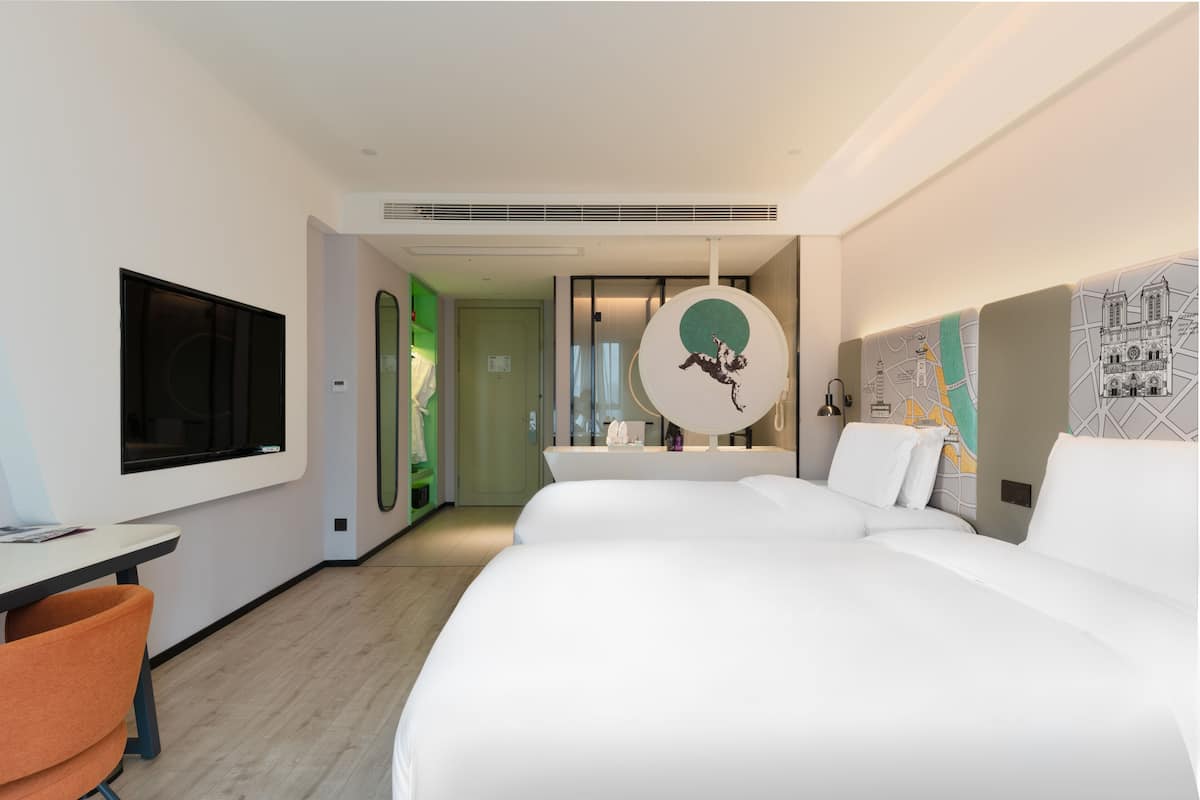 A hotel room with a bed, a desk, a chair, a TV, and a bathroom with a mirror.