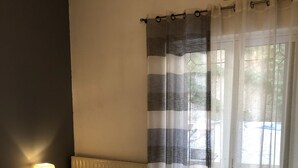 A hotel room with a bed, a nightstand with a lamp, a window with curtains, and an air conditioning unit. - Rosy's House (Χανιά)