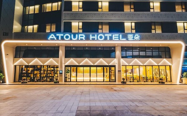 The exterior of Atour Hotel with a modern facade, large glass windows, and a prominent neon sign. - Atour Hotel (Nanjing)