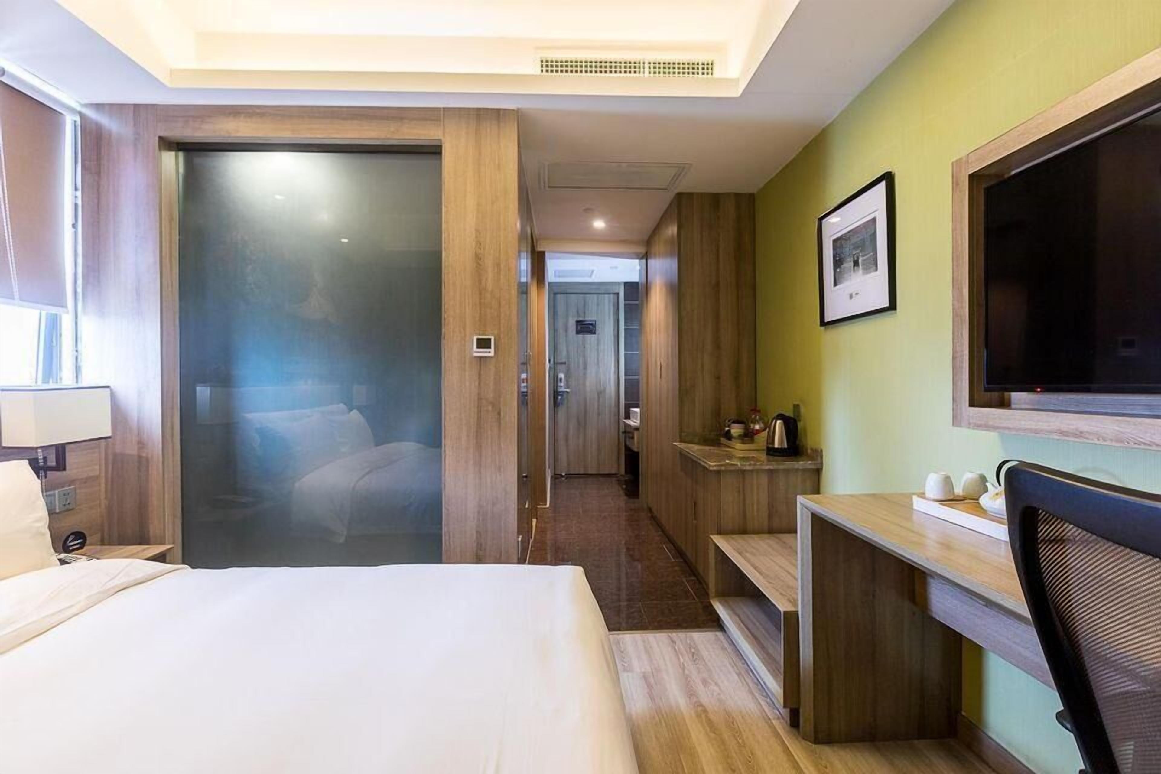 Hotelkamer met een bed, bureau, stoel, televisie en een badkamer zichtbaar door een glazen deur.